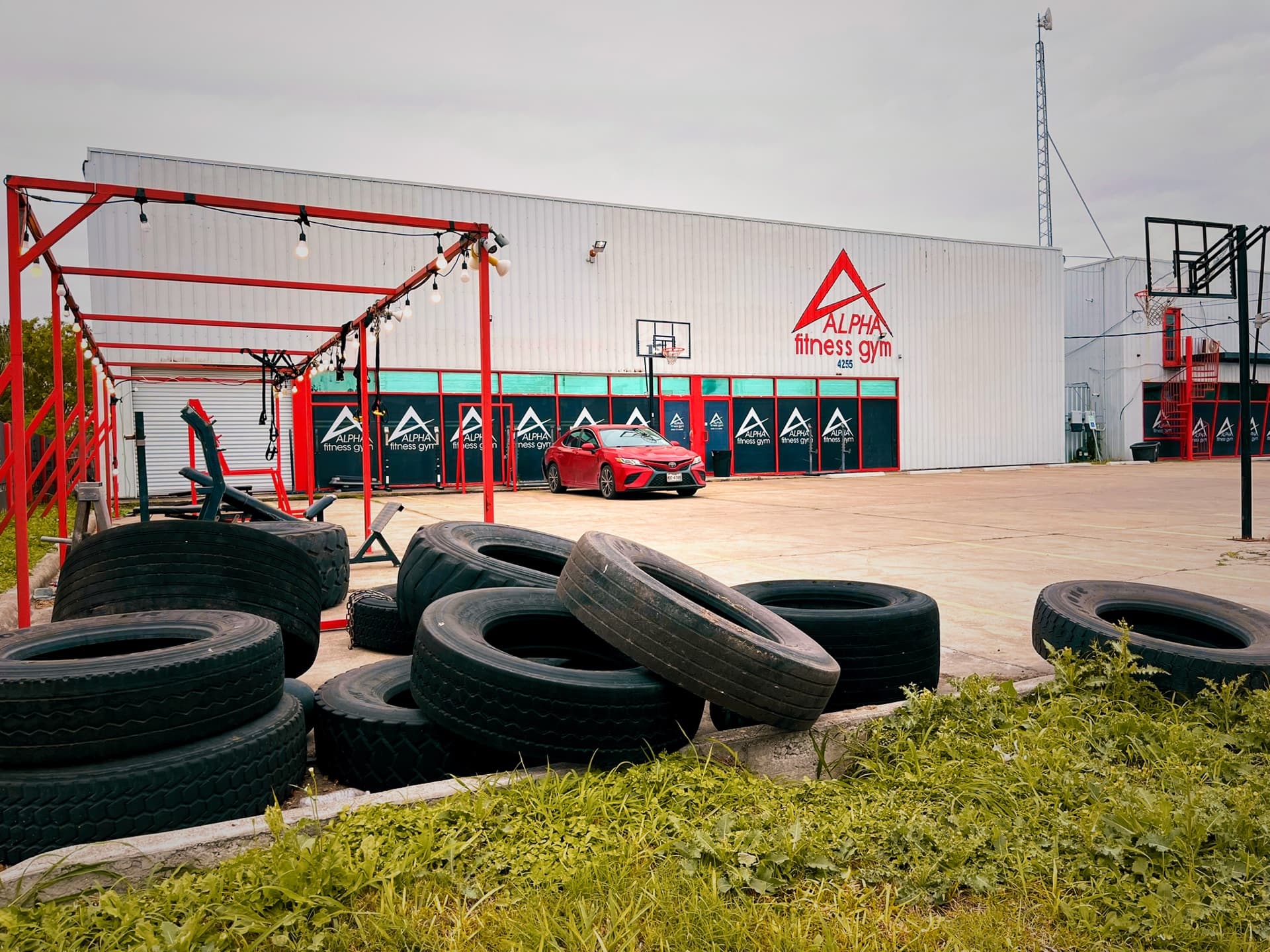 Outdoor training yard with red steel rigs, stacked tractor tires and a basketball hoop